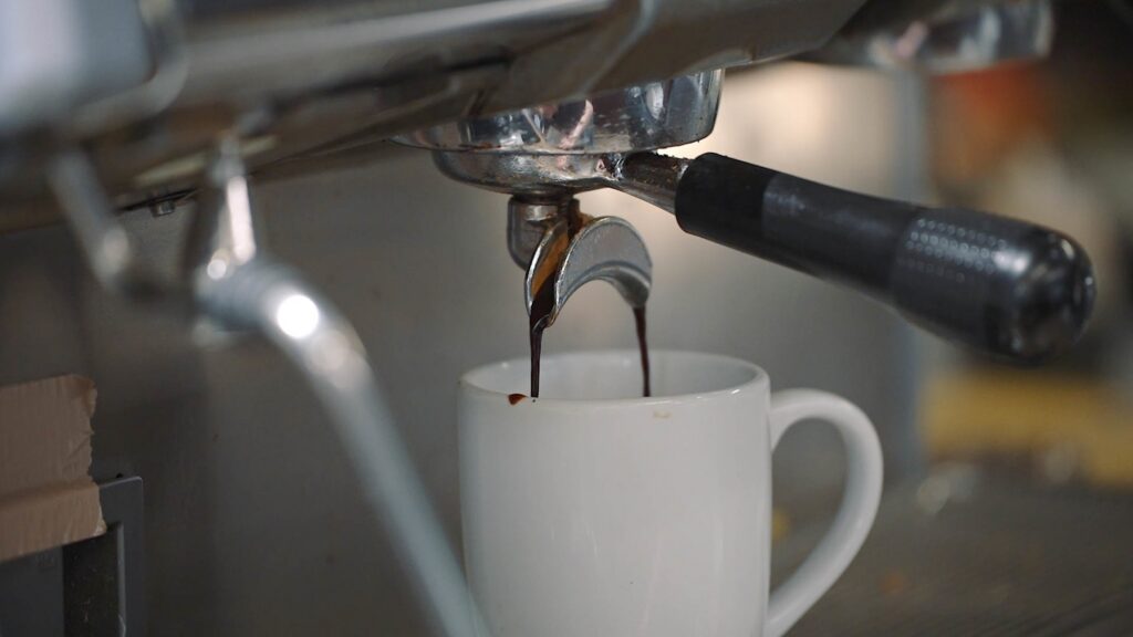 Espresso pouring in two streams from a portafilter spout into a white ceramic mug beneath an espresso machine group head.
